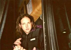 a man with long hair wearing a black jacket and holding something in his right hand