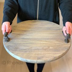 a person holding a round wooden table with black handles