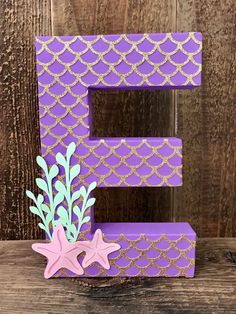 the letter e is made out of purple paper with gold and pink decorations on it