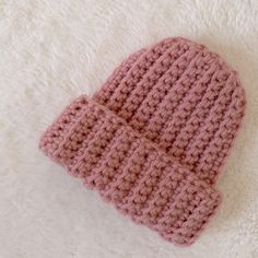 a pink crocheted hat laying on top of a white blanket