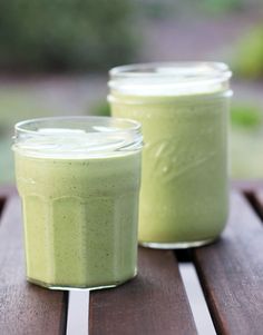 two jars filled with green smoothie sitting on top of a wooden table next to each other