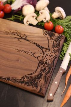 a cutting board with a tree on it next to carrots and other veggies