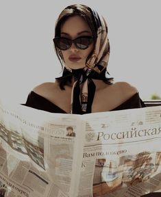 a woman wearing sunglasses and a scarf reading a newspaper