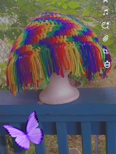 a purple butterfly sitting on top of a wooden table next to a white vase filled with colorful yarn