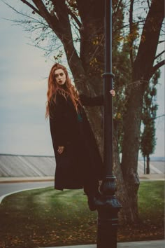 a woman standing on top of a street light next to a tree in the fall