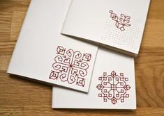 three cards with red designs on them sitting on a table next to some scissors and thread