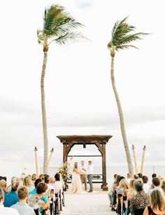 a wedding ceremony on the beach with palm trees and bride and groom standing at the alter