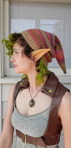 a woman with green hair wearing a brown hat and leather vest, standing in front of a window