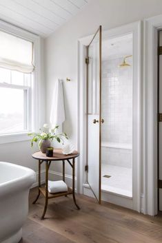 a bath room with a stand up shower next to a tub and a table in front of a window