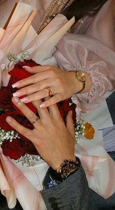 two hands on top of each other with wedding rings and flowers in front of them