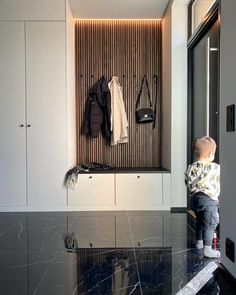 a little boy standing in front of a black and white wall with coat hooks on it