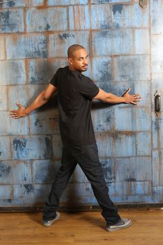 a man standing in front of a blue wall with his hands out to the side