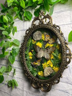 an ornate frame with butterflies and flowers in it on a white surface surrounded by green leaves