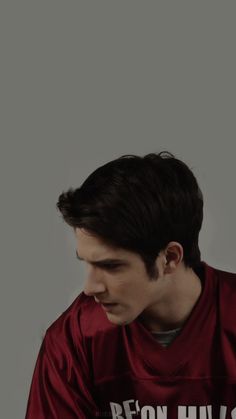 a young man sitting down with his hands on his knees, wearing a red shirt