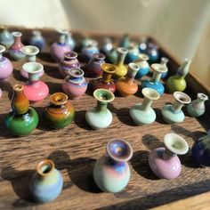 many small vases are sitting on a wooden table top, all different colors and sizes