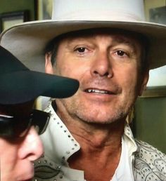 a man in a cowboy hat and sunglasses is talking to another person with a microphone