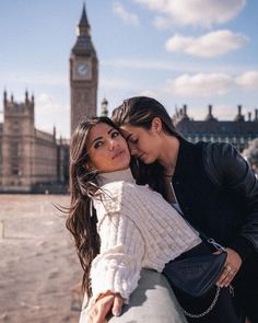 two beautiful women standing next to each other in front of a building with a clock tower