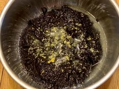 a metal bowl filled with black stuff on top of a wooden table next to a knife