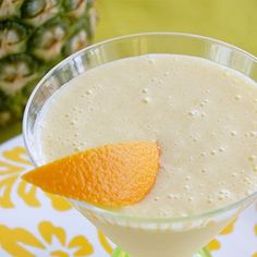 a drink in a martini glass with an orange peel on the rim next to a pineapple