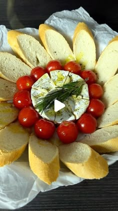 a flower shaped platter filled with bread, tomatoes and crackers on top of white paper