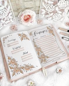 an open planner book sitting on top of a white blanket next to flowers and pens