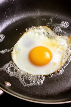 an egg frying in a skillet with water on the side and bubbles around it