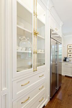 a kitchen with white cabinets and gold handles on the glass doored refrigerator freezer