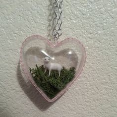 a glass heart with a small white sheep in it on a chain hanging from the wall