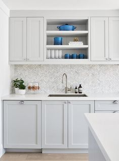 a kitchen with white cabinets and blue pots on the shelf above the sink is shown