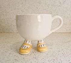 a white coffee cup with yellow feet sitting on top of it