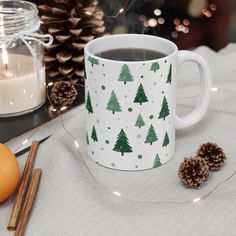 a coffee mug with christmas trees on it next to some cinnamon sticks and an orange