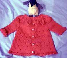 a stuffed animal sitting on top of a bed next to a knitted sweater with ruffles