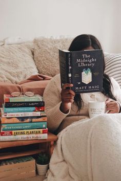 a woman sitting on a couch holding a book in her hands and reading it to the camera