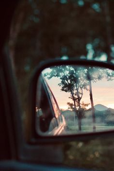 the side mirror of a car with trees and mountains in the backgrouund