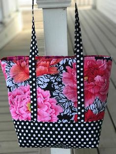 a black and white polka dot bag with pink flowers on the front is hanging from a pole