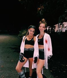 two young women dressed in sports wear posing for a photo outside at night with blood on the ground