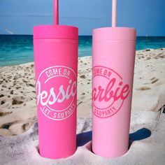 two pink tumblers sitting on top of a sandy beach