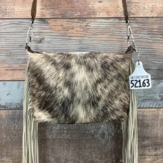 a brown and white cowhide purse with fringes hanging from it's side