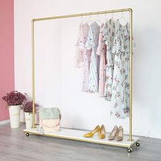 a rack with clothes and shoes on it in front of a pink wall