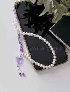 a cell phone with a white beaded necklace next to a book and flower pot