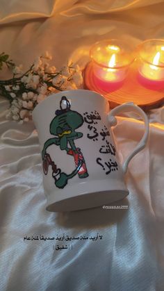 two lit candles sit next to a coffee cup with an image of a frog on it