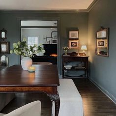 a dining room table with white chairs and pictures on the wall behind it in front of a mirror