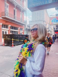 a woman standing on the sidewalk with her arms around her chest wearing a colorful feathered scarf