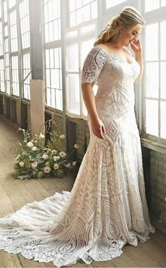 a woman standing in front of a window wearing a wedding dress with an off the shoulder design