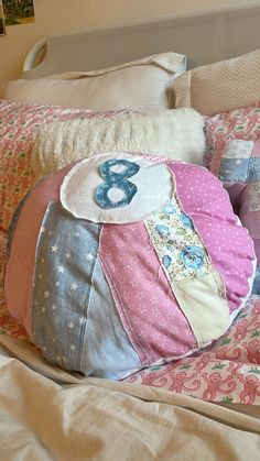 a large pillow on top of a bed covered in pink and blue pillows with numbers