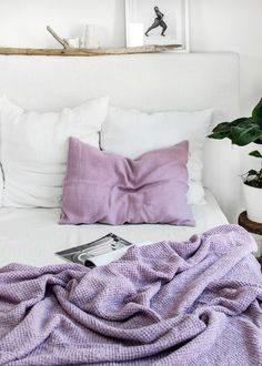 a white bed topped with pillows and blankets next to a potted plant on top of a wooden table