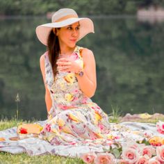 a woman wearing a hat sitting on top of a grass covered field next to flowers