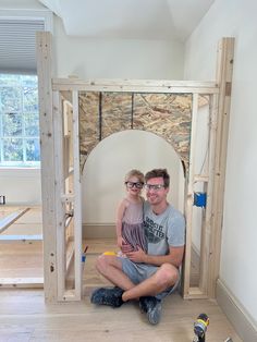 a man and woman sitting on the floor in front of an unfinished room with wood framing