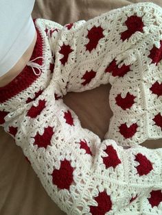 a crocheted red and white scarf on top of a bed next to a person's leg