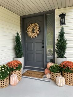 the front porch is decorated for fall with pumpkins and muminate plants in baskets